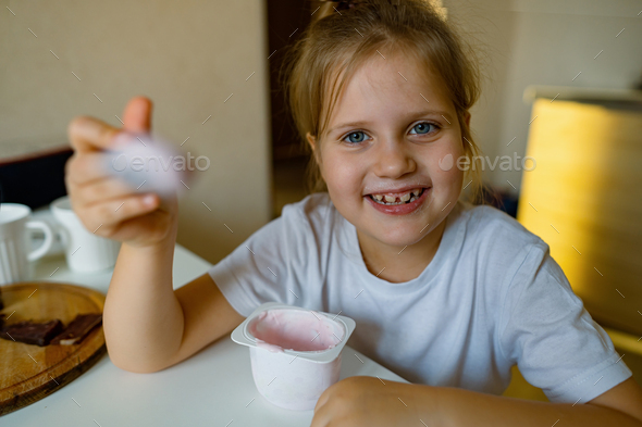 Cute girl eats yogur with appetite, has dirty mouth, has fun, grimaces