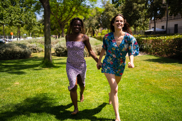 Two Women Of Different Ethnicities Running Holding Hands Outdoors Stock