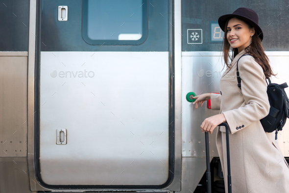 Cheerful woman presses button on the train door to enter. Railway trip concept