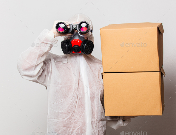 female postman in protection suit and glasses with mask holds delivery boxes and binoculars