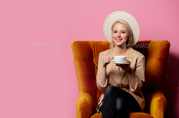 woman in cowboy hat sitting in a vintage armchair with cup