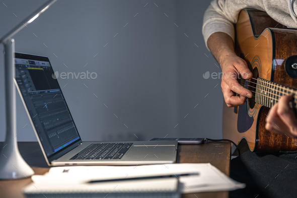 A man with a guitar in front of a laptop at a late hour learns to play.