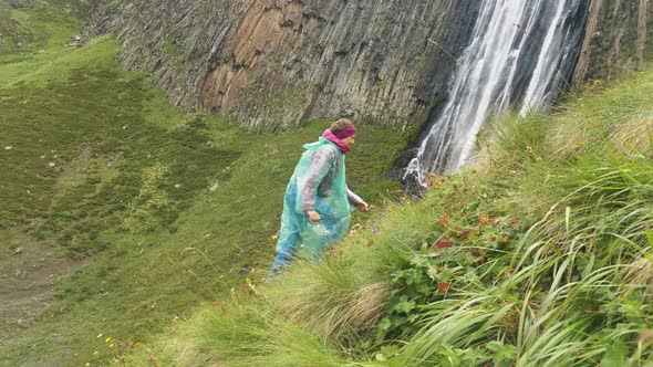 Sports Woman Traveler in a Raincoat Runs Up the Green Mountain Slope Against the Backdrop of a alt