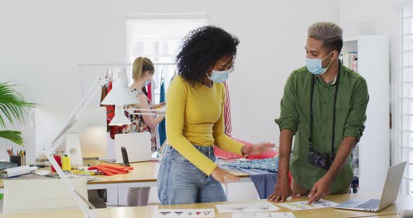 Female fashion designer and male photographer wearing face mask discussing with each other in studio alt