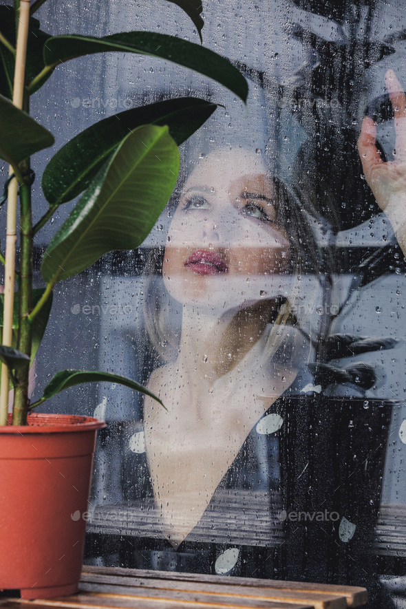 woman near wet window after the rain misses the ficus plant standing outside the window.