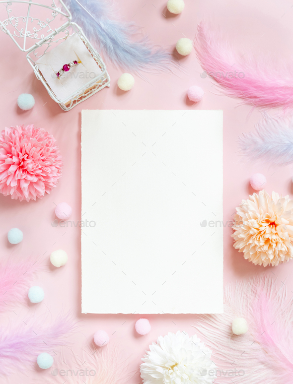 Blank Card near pastel flowers, pom-poms, feathers and ring in a gift box on pink