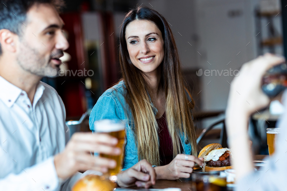 Attractive young friends group eating burgers while talking and having fun in the restaurant.