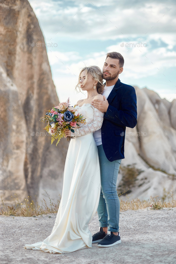 Woman in long white dress with bouquet of flowers in her hands, man in jacket. Wedding
