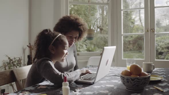 Mother with daughter teaching on laptop in kitchen