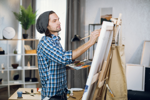 Man in casual wear painting on easel in studio