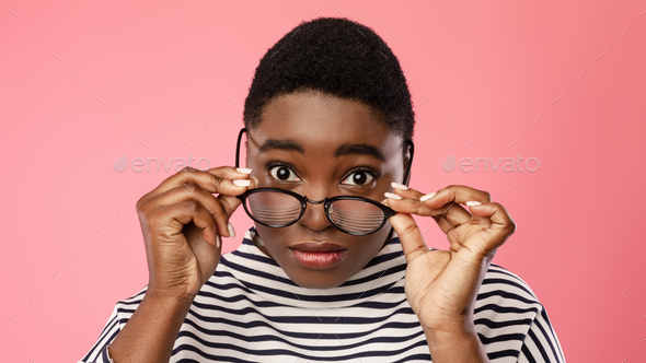 Black Woman Looking At Camera Above Eyeglasses Over Pink Background