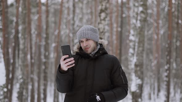 Happy Man in Winter Clothes Holds Smartphone Makes Video Calls with Friends alt
