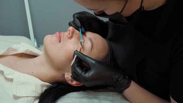 the Eyelash Extension Master Leans Over the Client and Combs the Eyelashes with a Special Brush alt