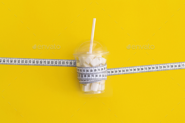 Measuring tape and sugar cubes on yellow background. Diabetes and weight loss concept
