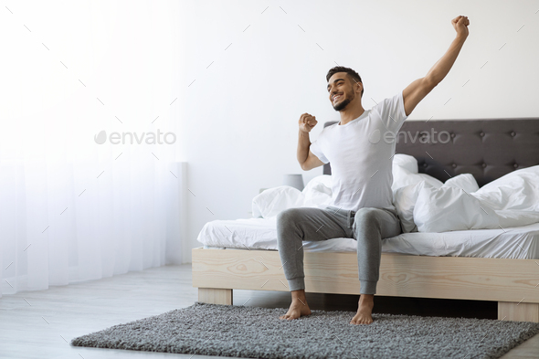 Good Morning. Happy Arab Guy Sitting On Bed And Stretching After Sleep