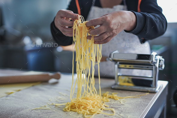 Senior woman working inside pasta factory and holding fesh made tagliatelle