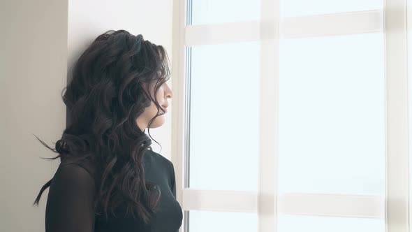 Side View Unhappy Woman with Long Hair Stands Near Window alt