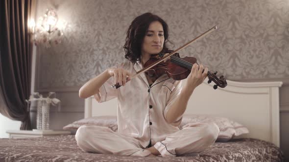 Beautiful Girl Playing the Violin While Sitting on the Bed at Home Handheld Shooting