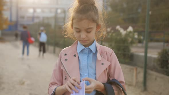 A School Girl Puts on a Protective Medical Mask and Heads Towards the School alt