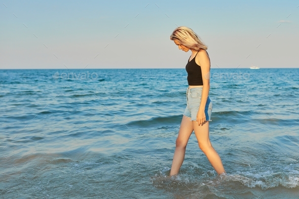 Beautiful young woman walking in profile on the water along sea beach