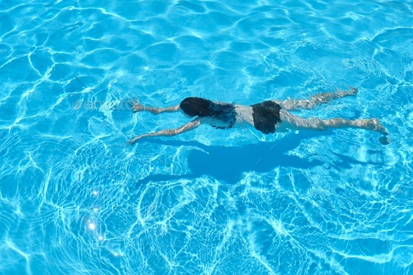 Young woman in bikini swimming underwater in an outdoor swimming pool, top view