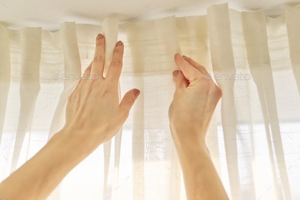 Close up of woman hands hanging curtain with metal hooks on ceiling ledge