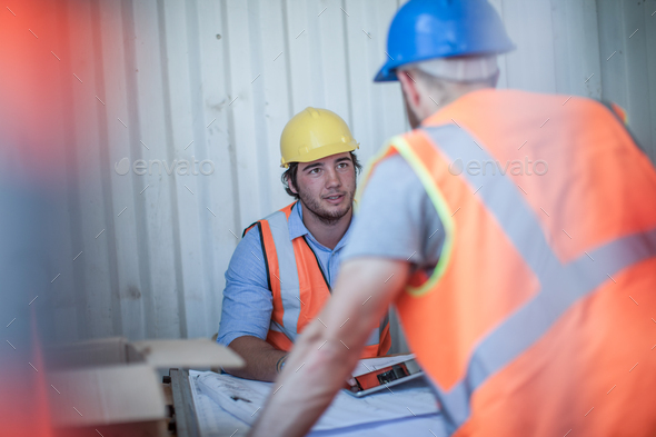 Site manager sitting at desk talking to worker in portable cabin