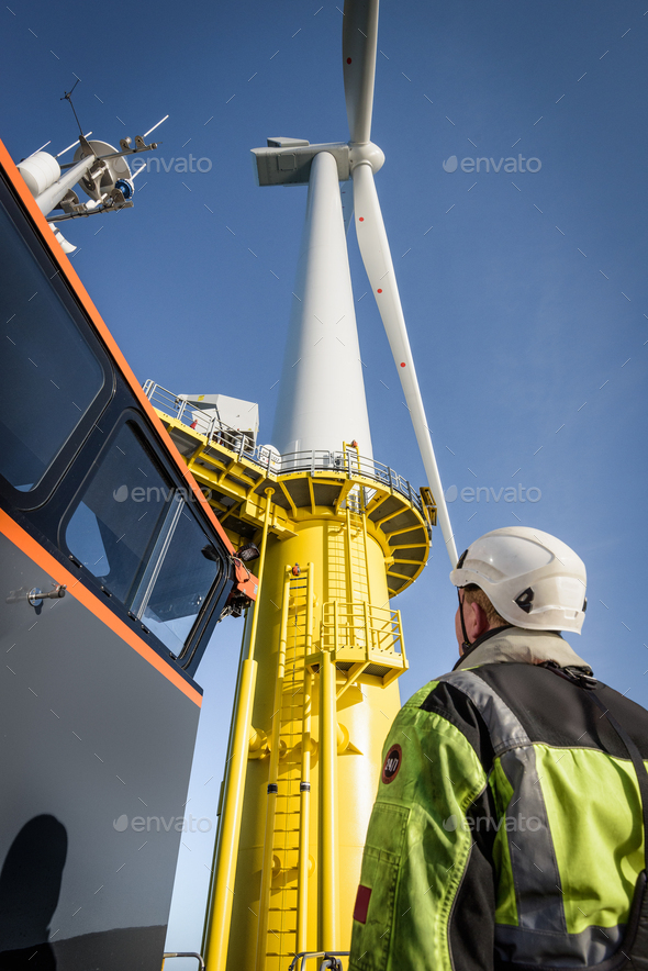 Engineers climbing wind turbine from boat at offshore windfarm, low