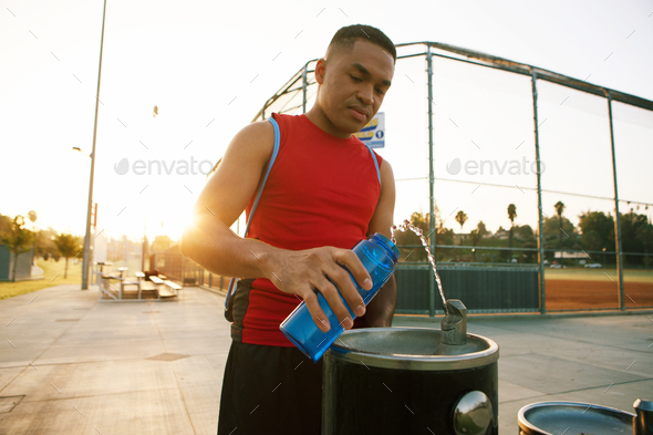 Young man filling water bottle from drinks fountain