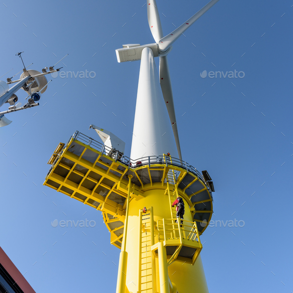 Engineer climbing wind turbine from boat at offshore windfarm, low angle view