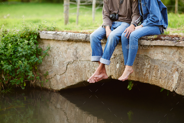 Neck down view of young couple sitting on river footbridge
