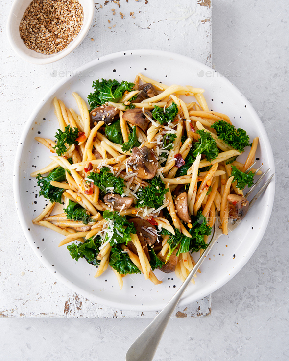 Whole grain pasta with kale, mushrooms, parmezan cheese in white plate.