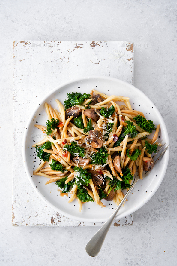 Whole grain pasta with kale, mushrooms, parmezan cheese in white plate.