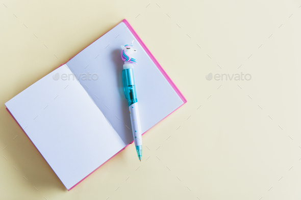 Pink notebook for notes, funny unicorn pen on yellow pastel background. Flat lay. Top view. Copy