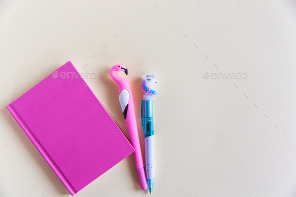 Pink notebook for notes, funny unicorn and flamingo pens on yellow pastel background. Flat lay. Top