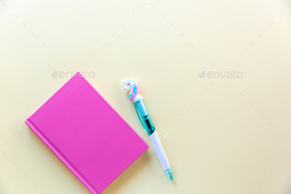 Pink notebook for notes, funny unicorn pen on yellow pastel background. Flat lay. Top view. Copy