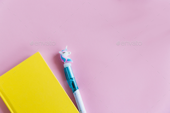 Yellow notebook for notes, funny unicorn pen on pink pastel background. Flat lay. Top view. Copy