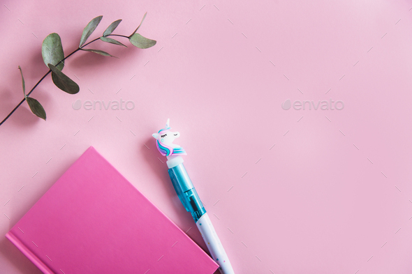 Pink notebook for notes, funny unicorn pen and green eucalyptus leaves on pink pastel background