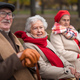 Group of happy senior friends sitting on bench in town park in autumn, looking at camera - PhotoDune Item for Sale