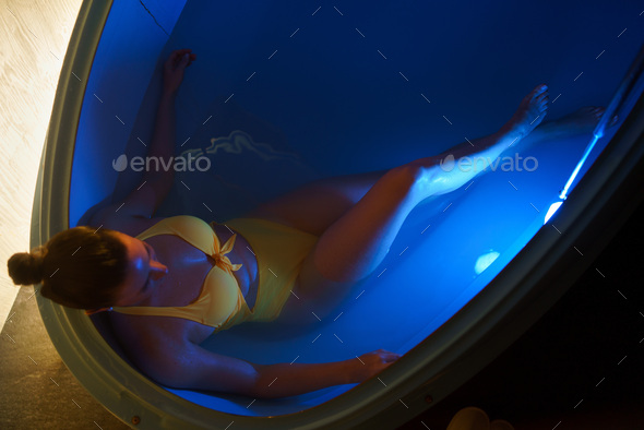Beautiful woman floating in tank filled with dense salt water used in medical therapy - Stock Photo - Images