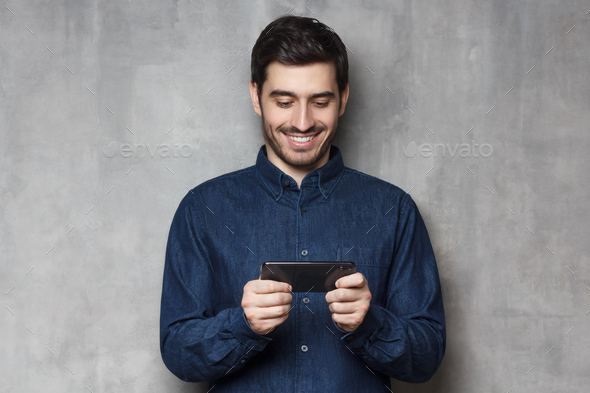 Handsome smiling man using his smartphone for gaming or watching video