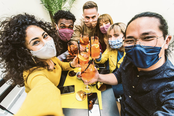 Happy friends wearing protective face masks taking selfie at restaurant