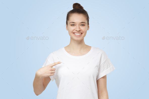 Young woman points with index finger at blank white t-shirt as if advising it to wear