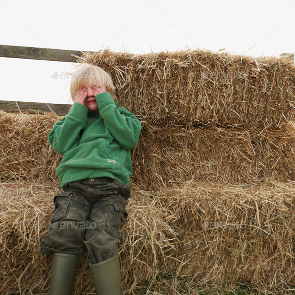 Boy hiding eyes on hay bales
