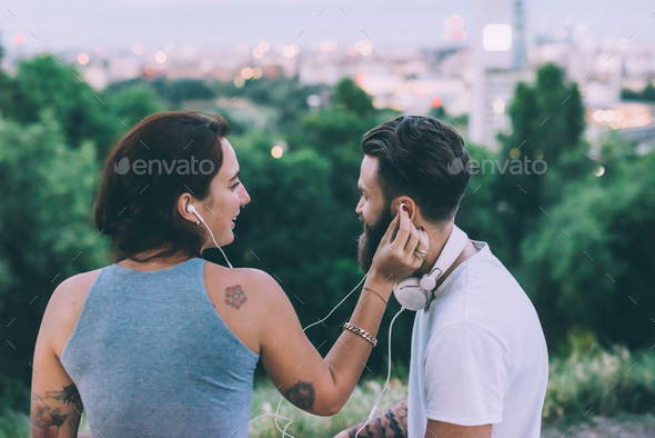 Young couple of lovers outdoor in the evening sharing earpods listening music