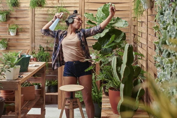 Happy young woman dancing on her terrace while gardening