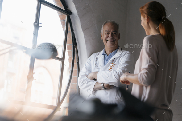 Smiling senior doctor talking to woman at the window in medical practice