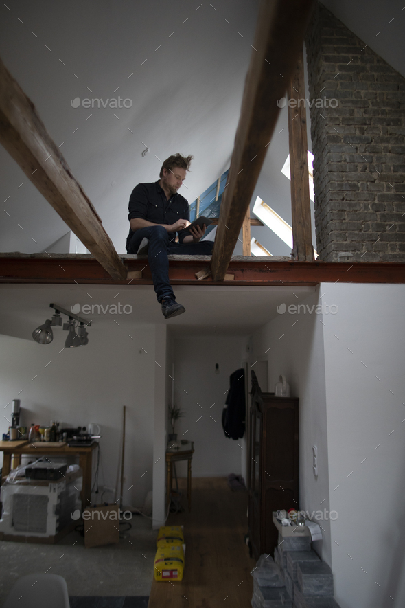 Architect working on construction sit of a loft conversion, sitting in truss