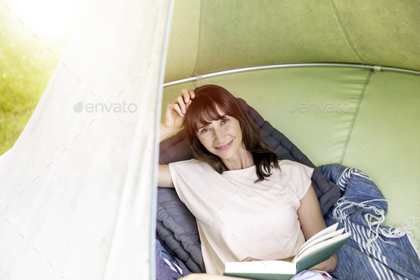 Portrait of smiling woman reading book in a hanging tent