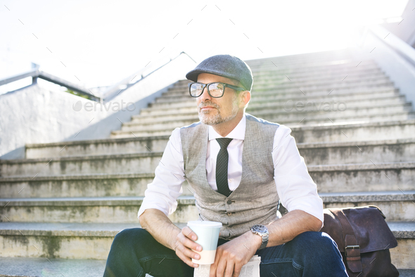 Businessman with coffee and newspaper in the city sitting on stairs